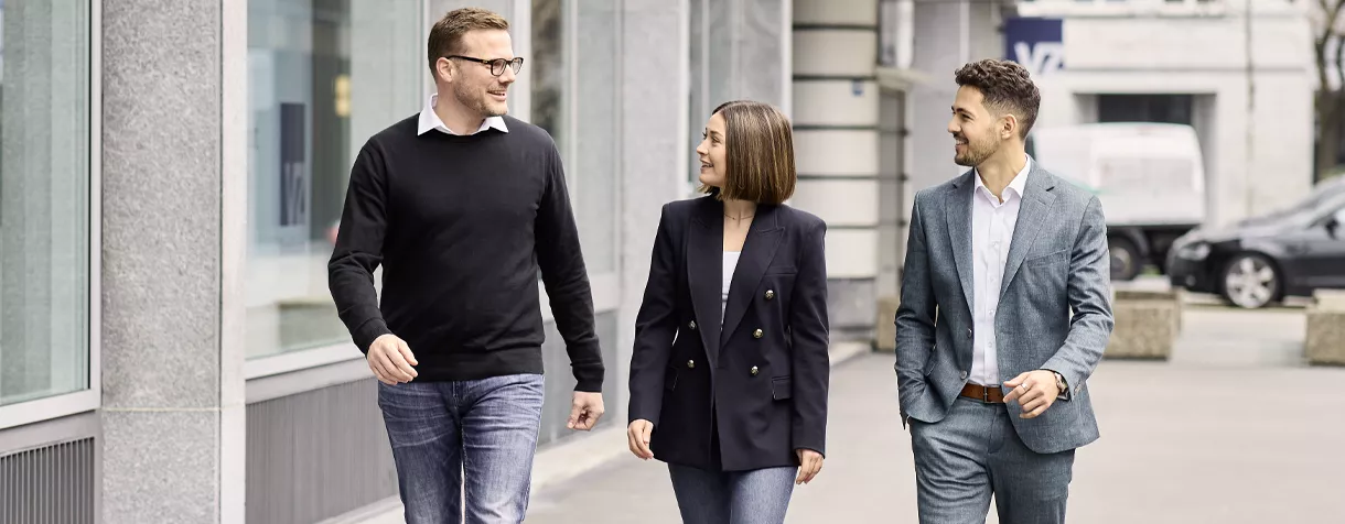 Das Bild zeigt drei VZ-Mitarbeiter während einer Unterhaltung nebeneinanderher laufend.